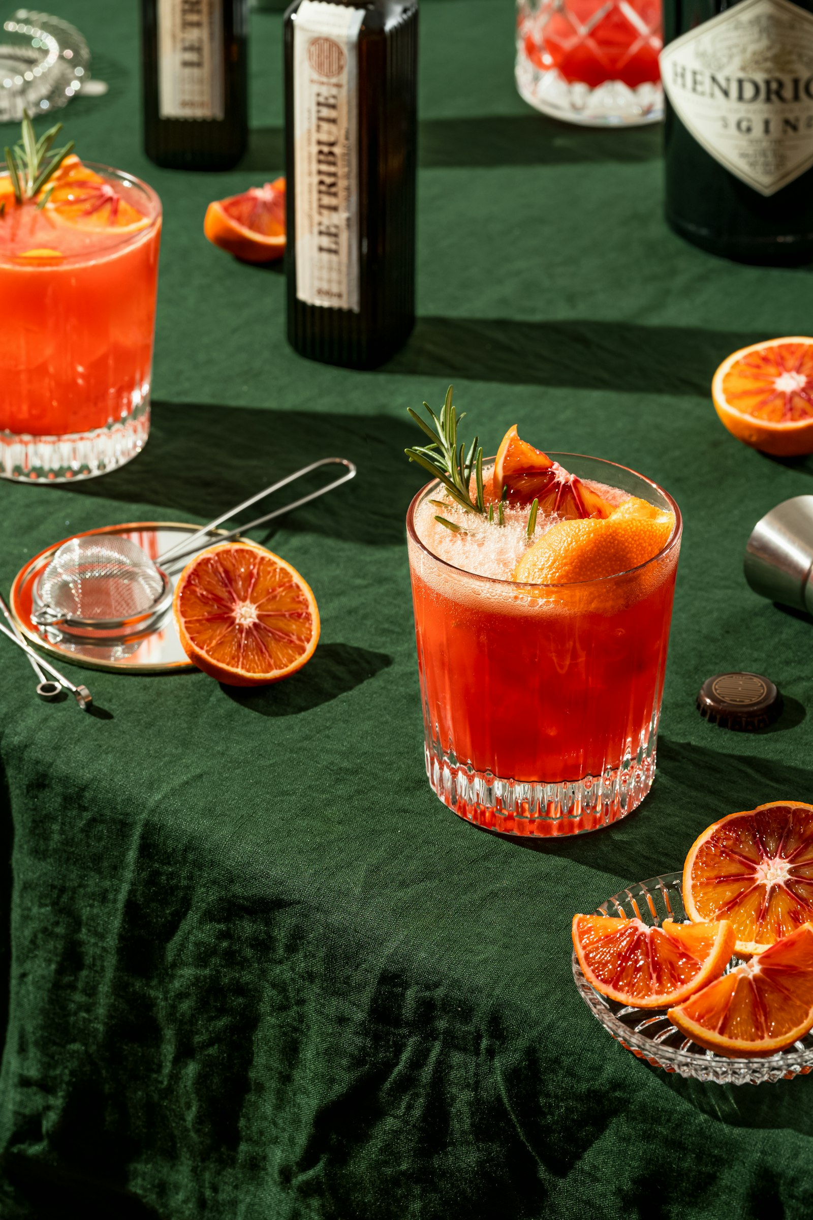 Blood orange cocktails with rosemary sprigs on a dark green linen tabl